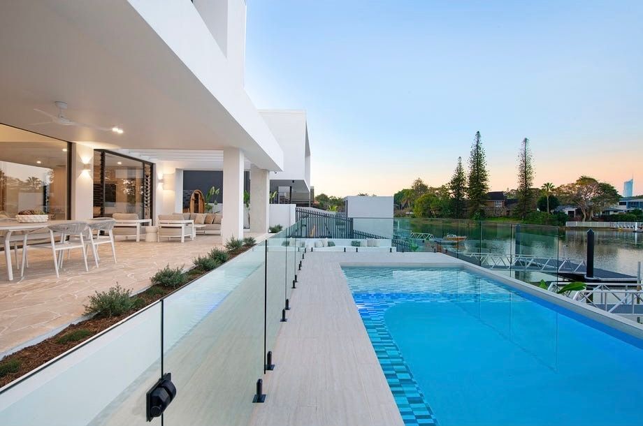 Modern patio with glass railing overlooking a blue swimming pool at sunset