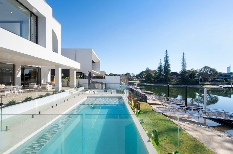 Modern white house with a turquoise pool and glass railing overlooking a waterfront view