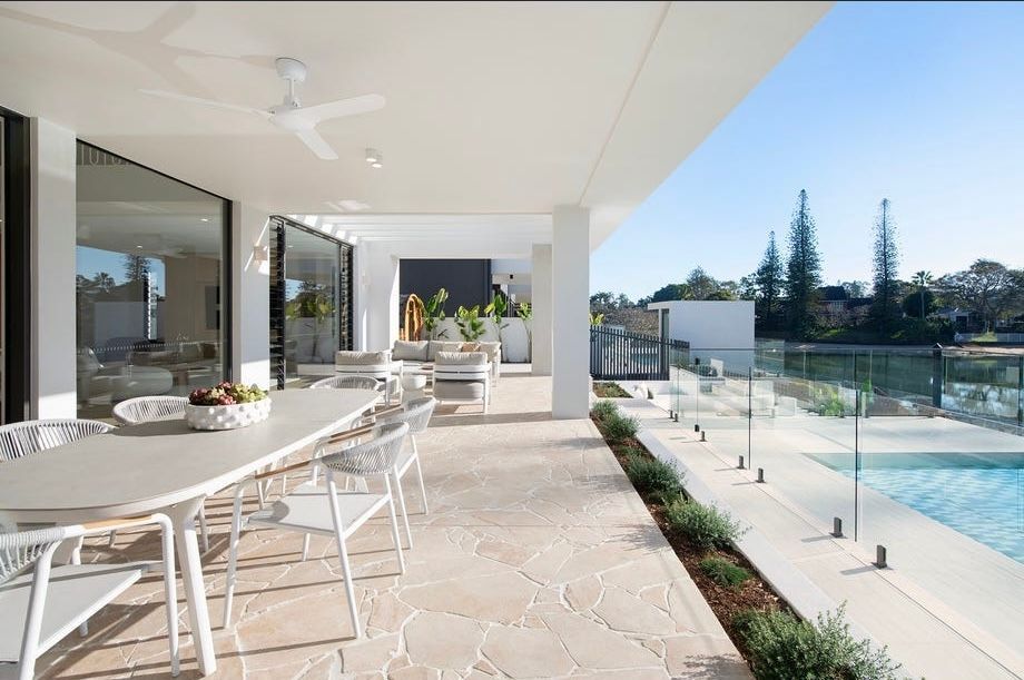 Modern patio dining area with white table, chairs, and poolside terrace overlooking the water