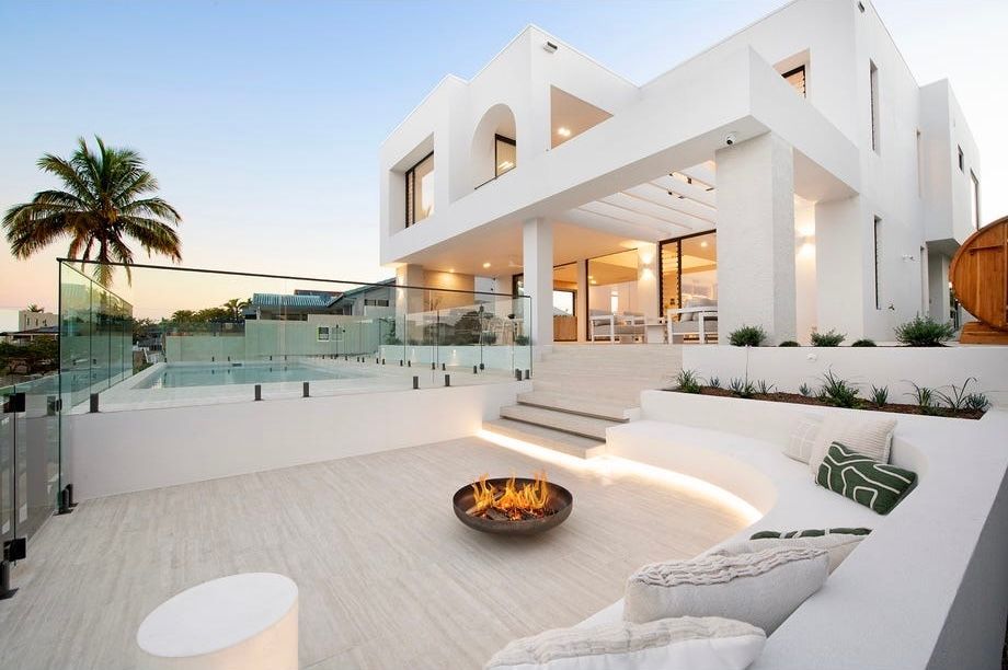 Modern white luxury villa patio with glass railing, fire pit, and sunset view