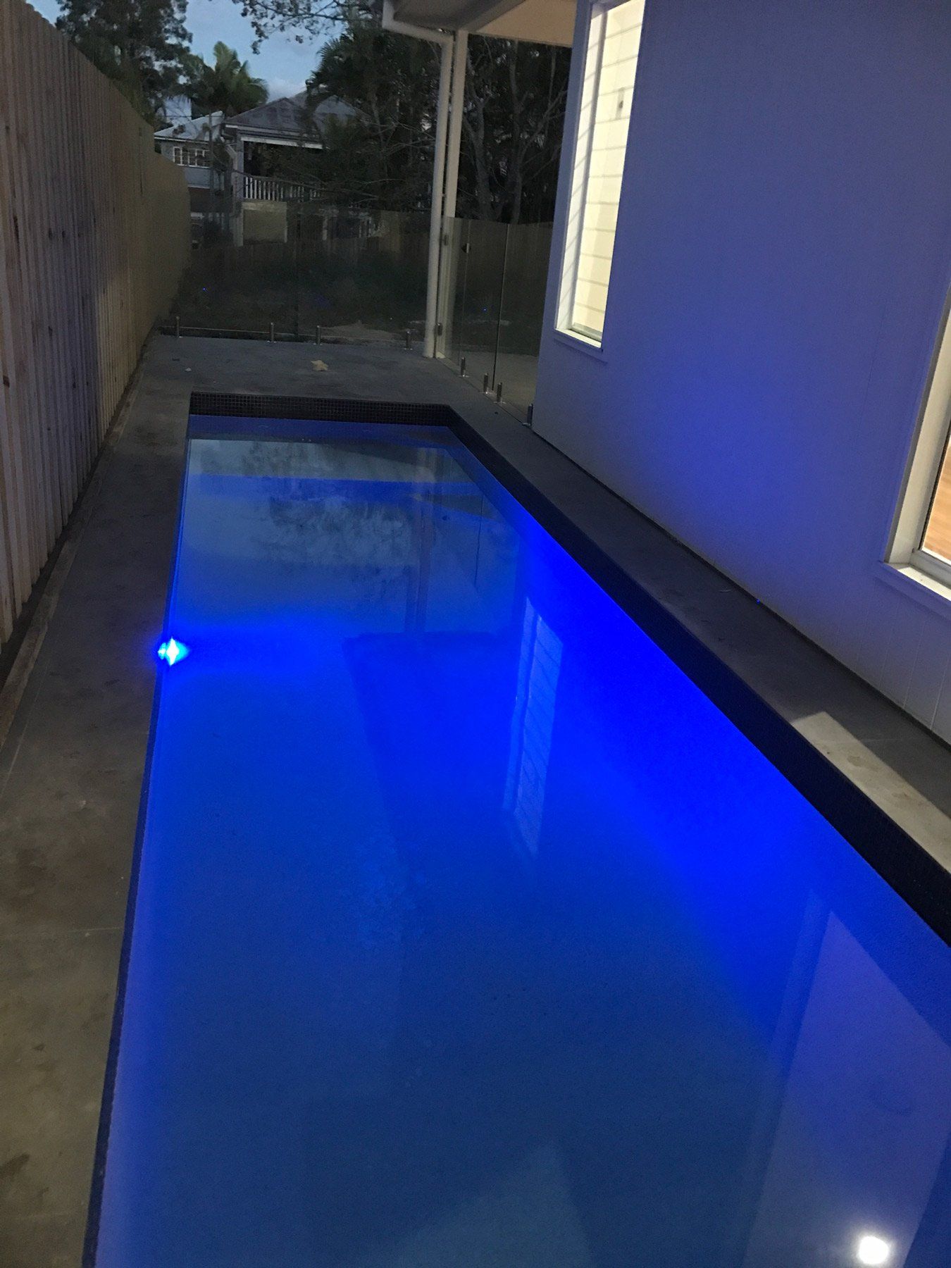 A narrow rectangular pool with bright blue water, reflecting light, beside a white wall.
