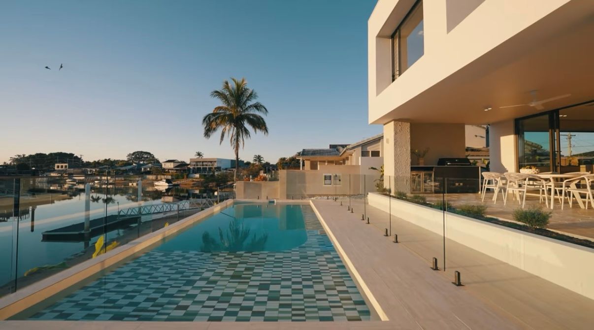 Modern waterfront pool terrace with turquoise pool, palm tree, and marina views at sunset