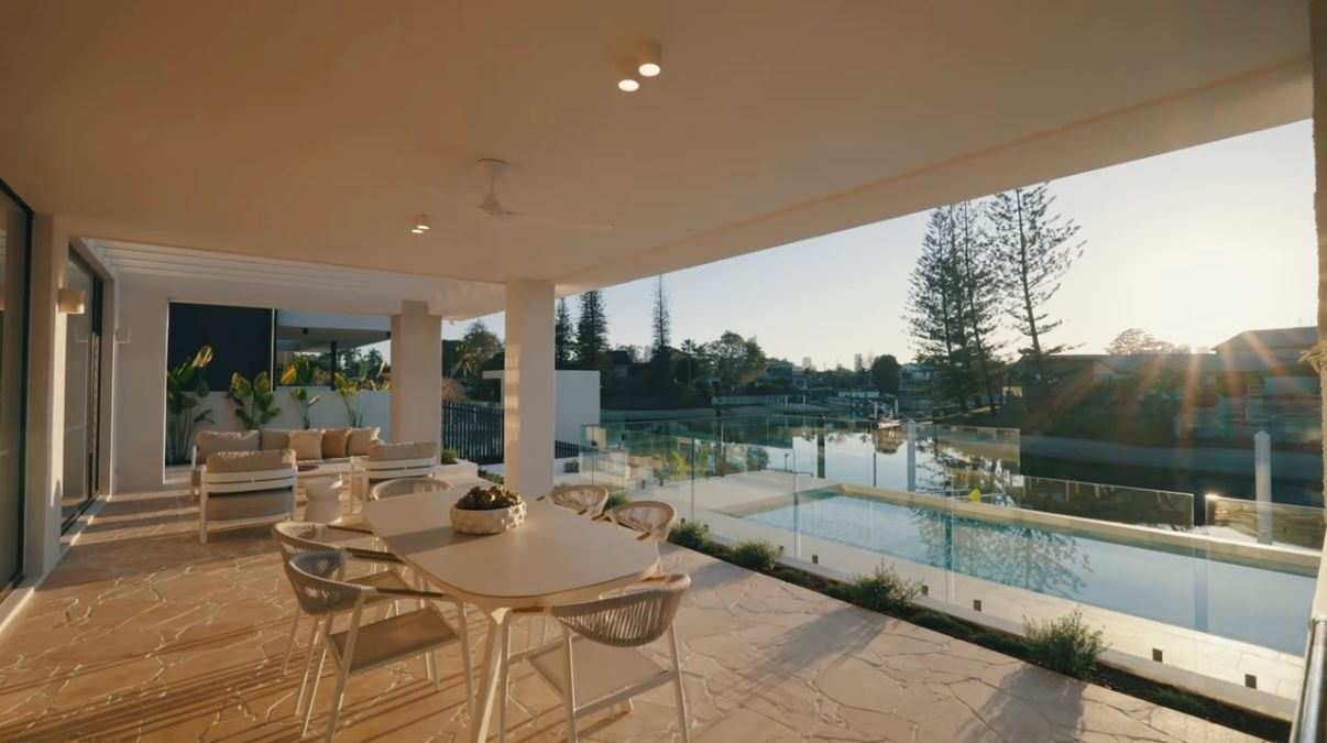 Sunlit patio with outdoor tables and chairs beside a pool and modern villa at sunset