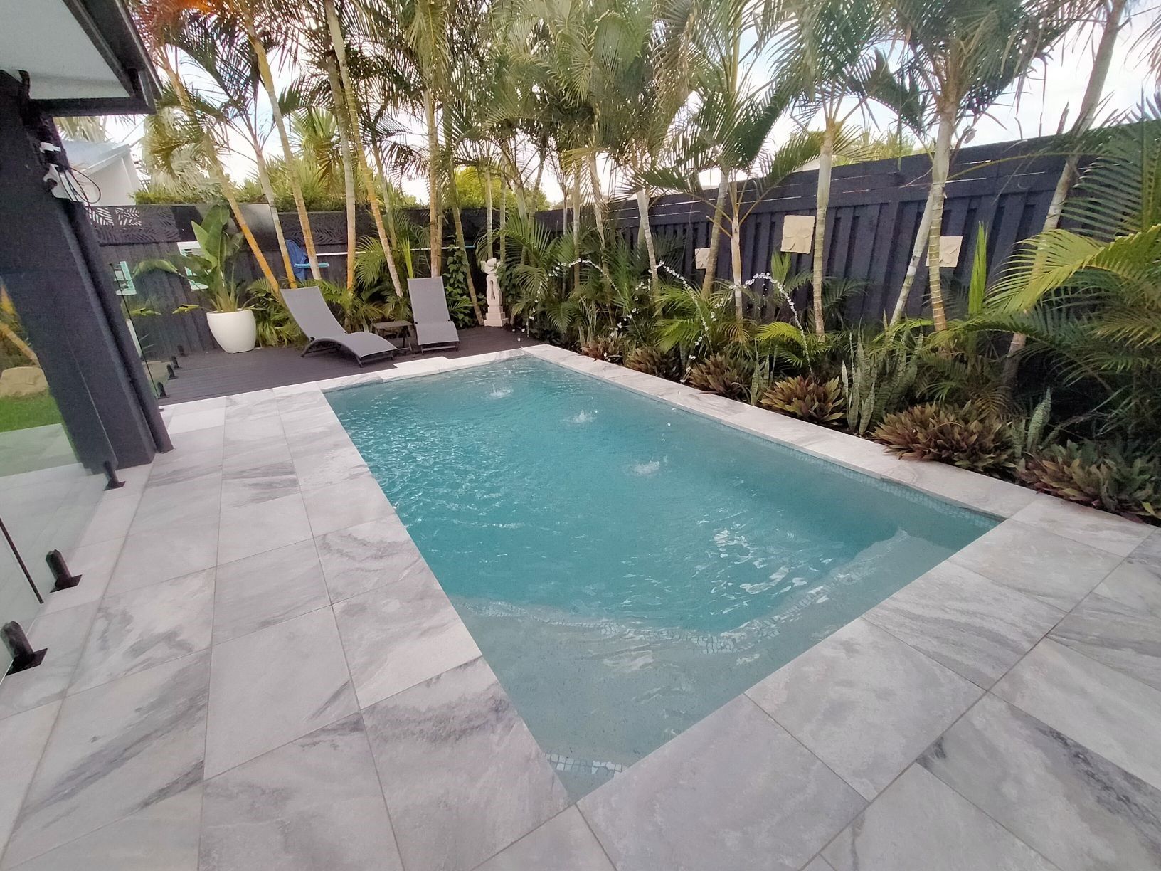 Pool with marble surround, flanked by greenery, and lounge chairs; exterior shot.