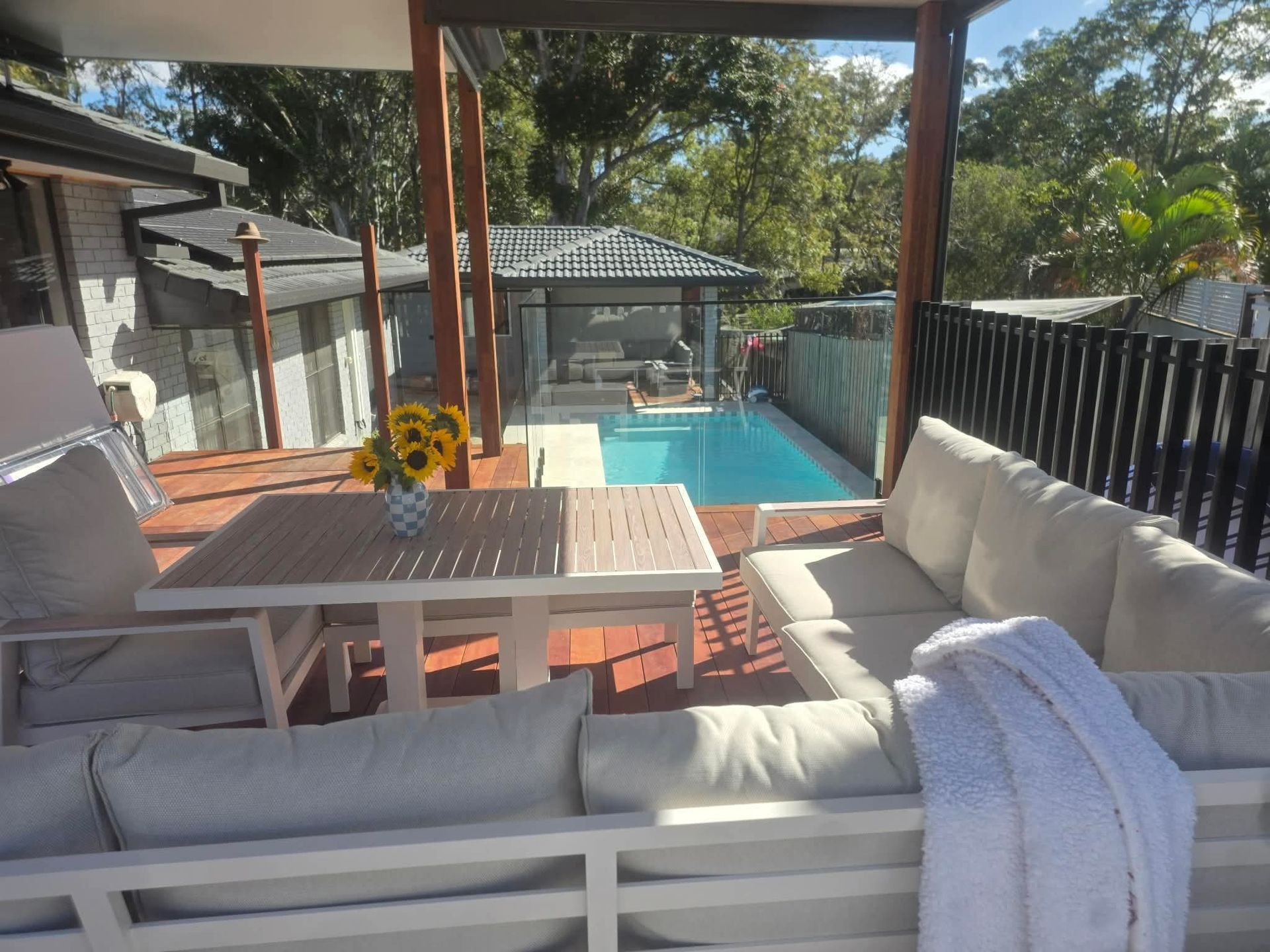 Covered patio seating overlooking a backyard pool, with white outdoor furniture and a table of sunflowers.