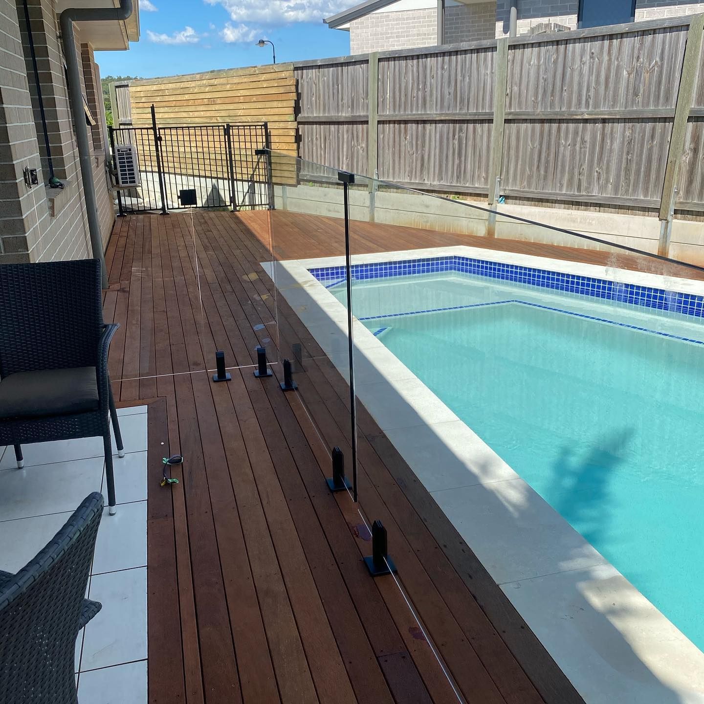 A wooden deck and swimming pool with glass fencing; blue water and light brown wood.