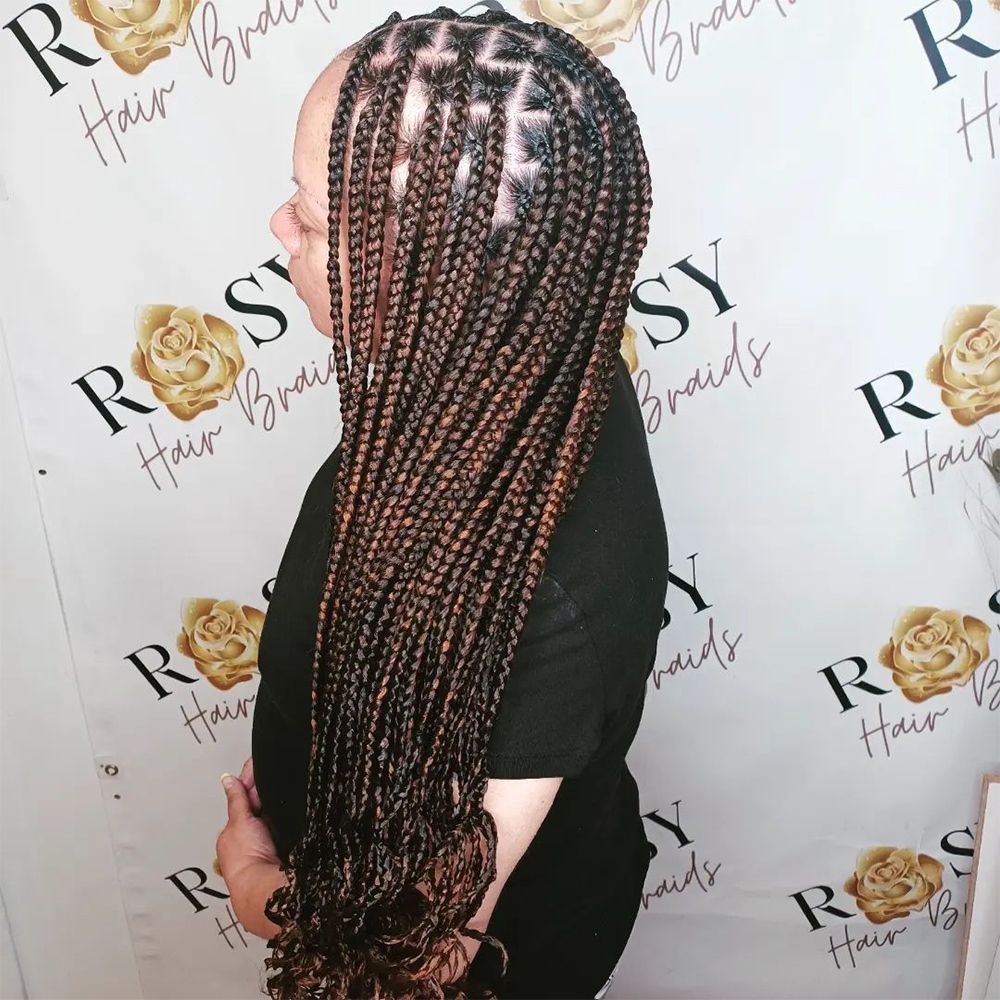 A woman with braids is standing in front of a sign that says rosy hair braids