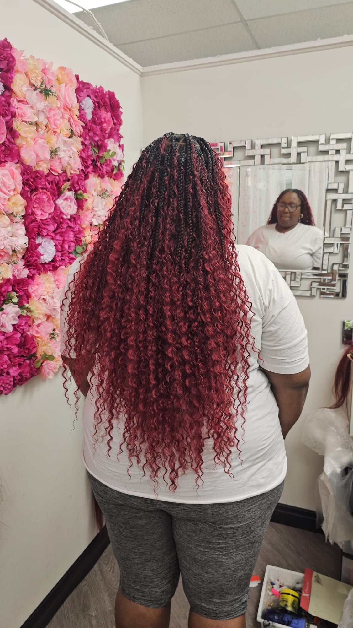 A woman with braids is standing in front of a wall that says rosy hair braids.
