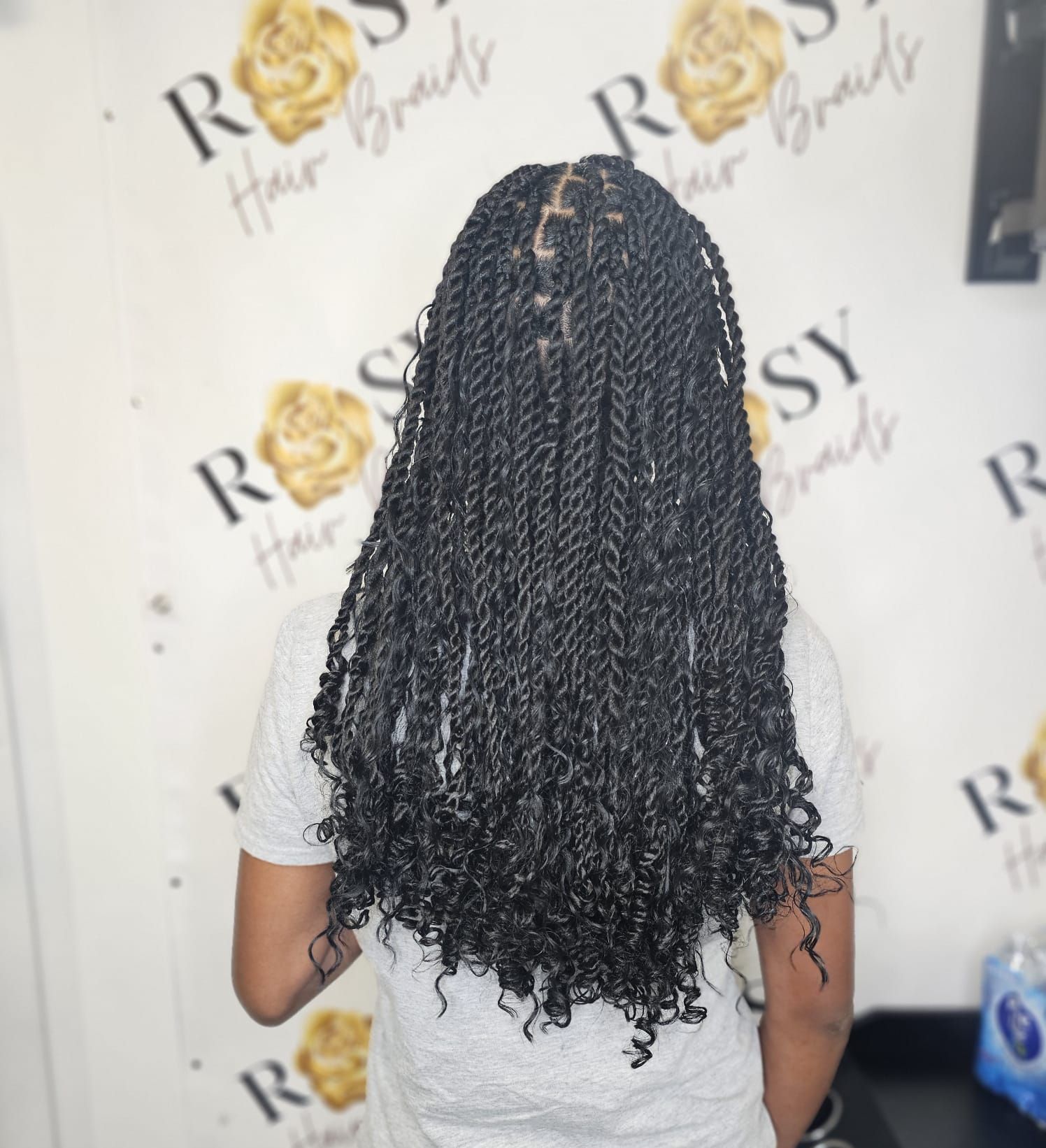 A woman with braids is sitting in a chair in front of a wall that says rosy
