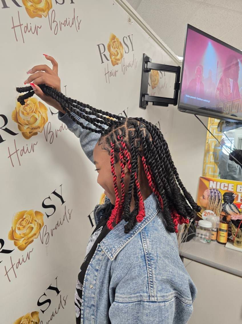 A person with black and red twist braids, wearing a denim jacket, raises their arm.