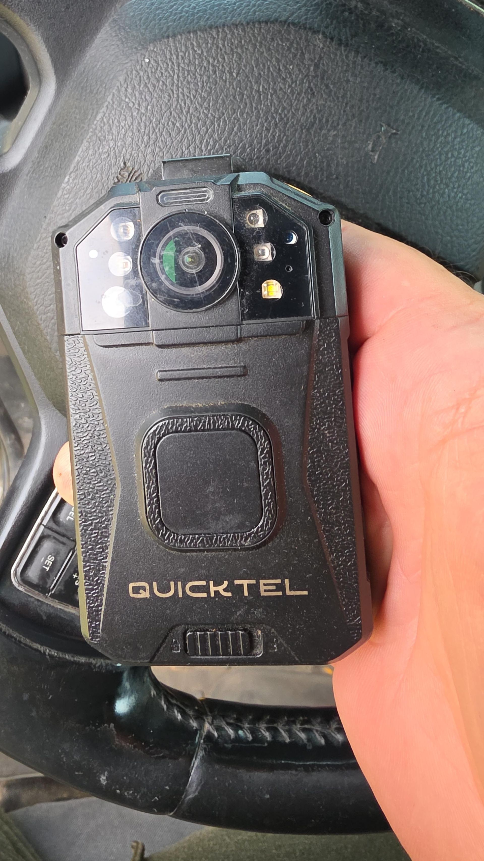 Black Quicktel handheld device with a camera and worn front panel, held in a hand inside a car.
