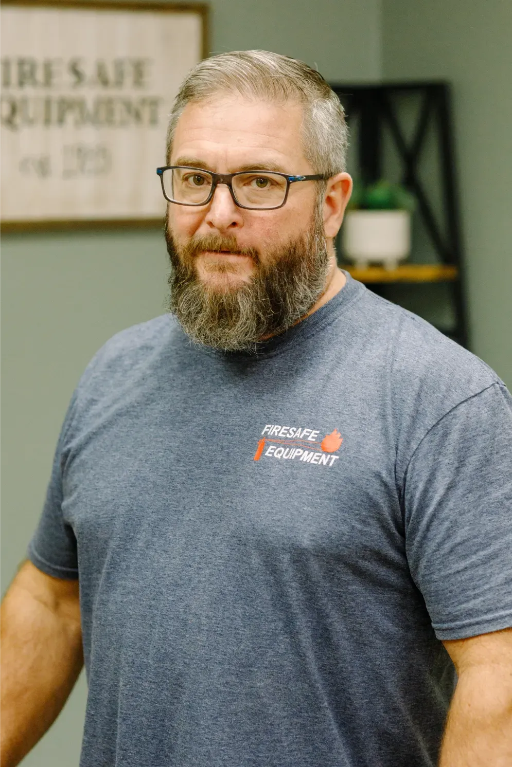 A man with a beard and glasses is wearing a blue t-shirt.