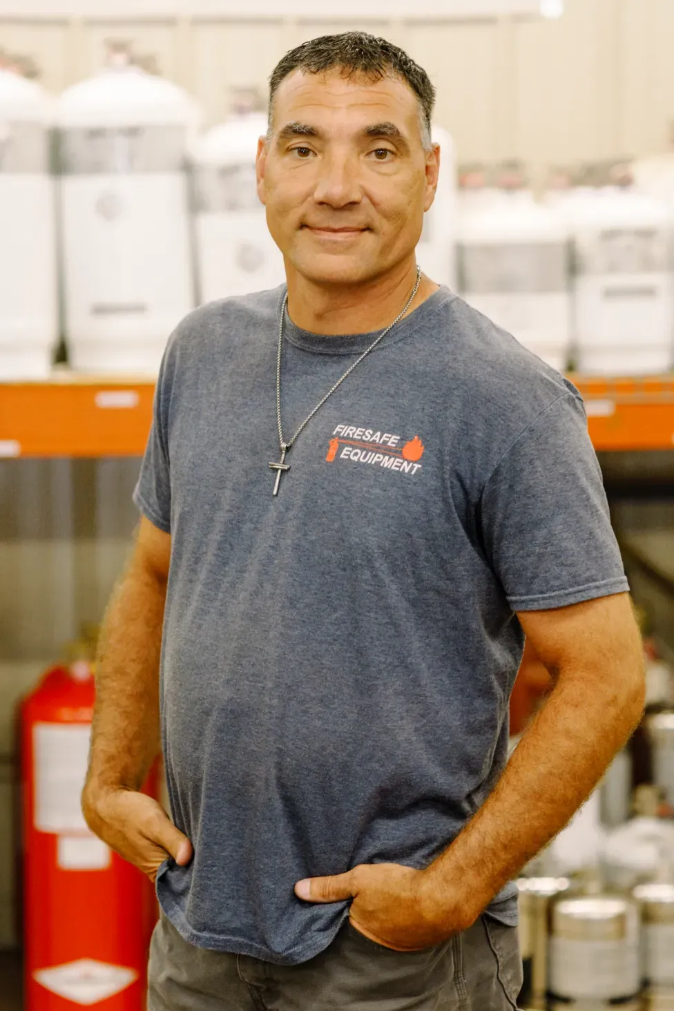 A man in a blue t-shirt is standing in front of a shelf with his hands in his pockets.