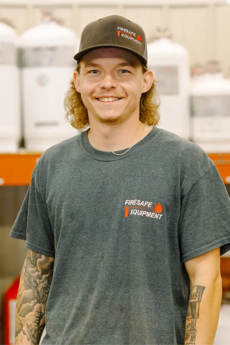 A man wearing a hat and a gray t-shirt is standing in front of a shelf.