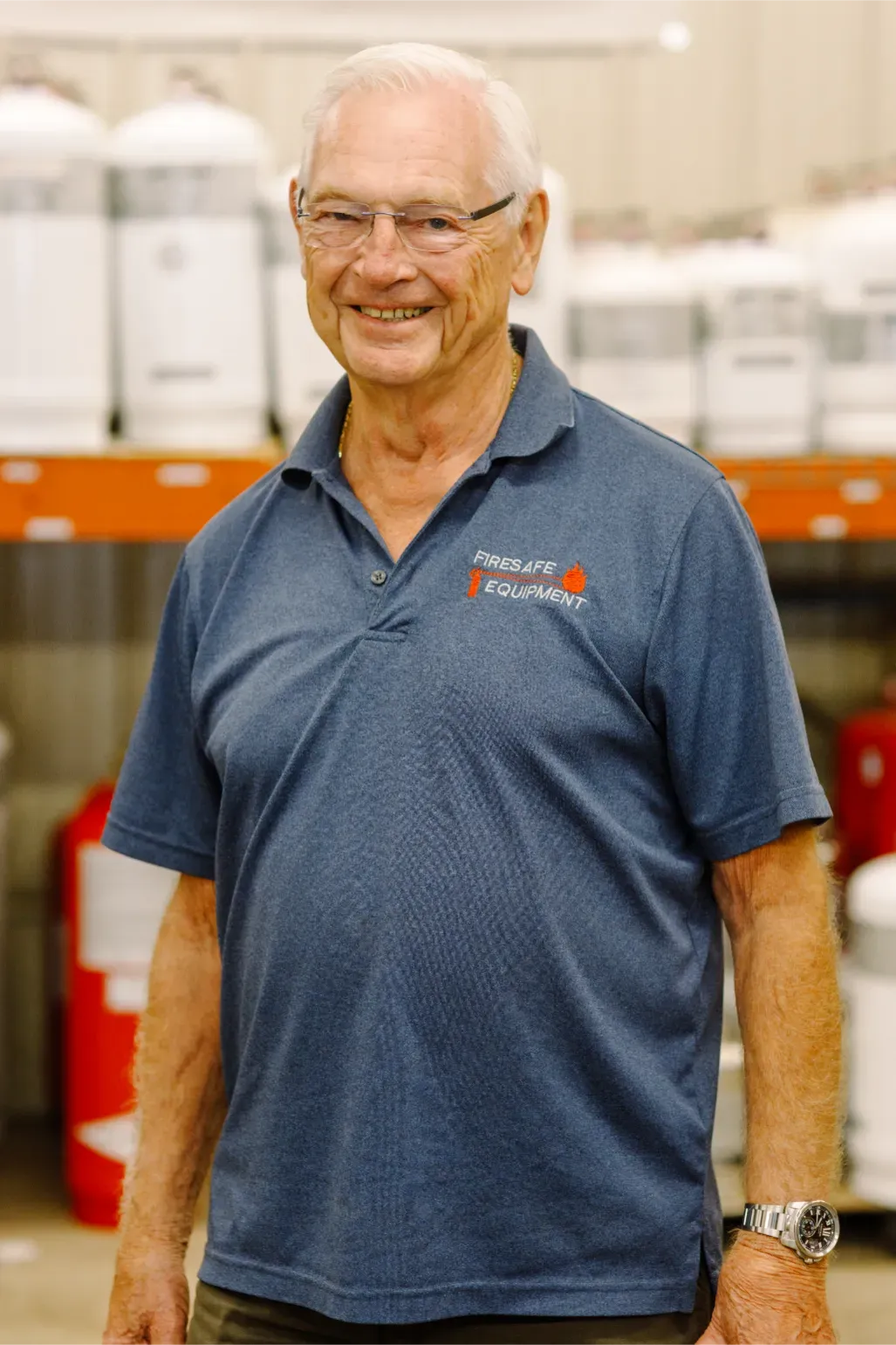 A man wearing a blue shirt and glasses is standing in a warehouse.