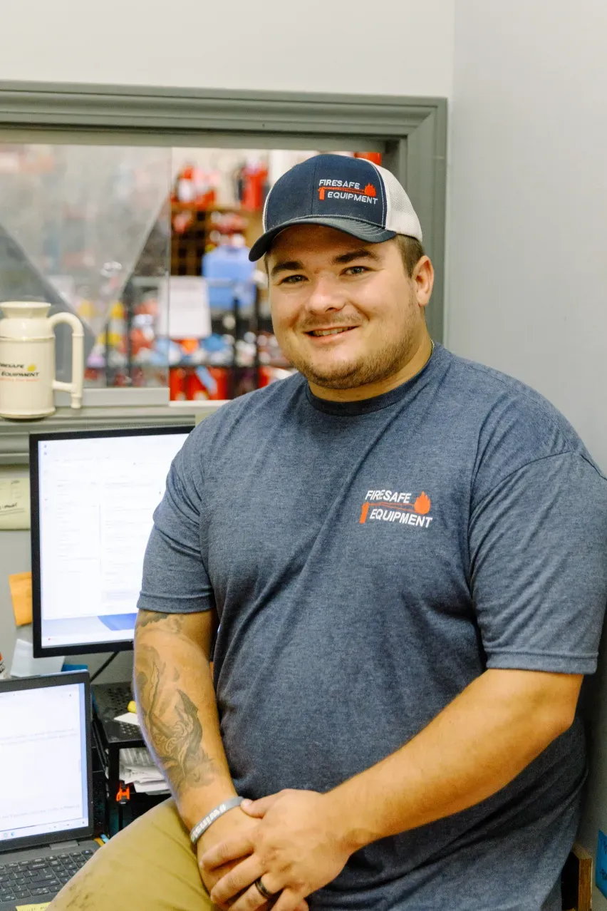 A man wearing a hat and a blue shirt is sitting in front of a computer.