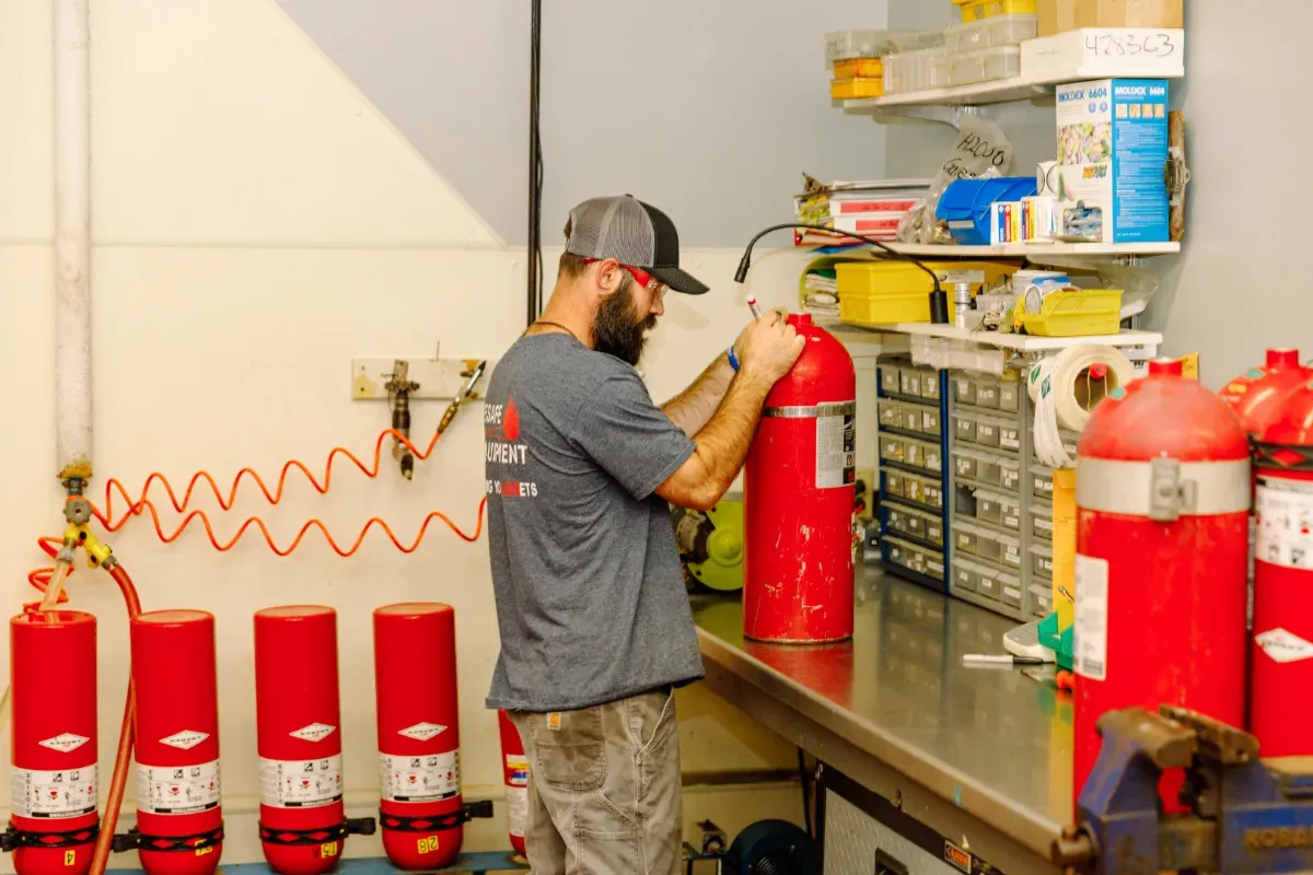 A man is working on a fire extinguisher in a workshop.