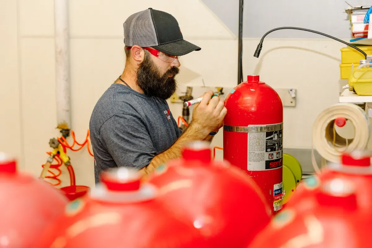 A man is working on a fire extinguisher in a room.
