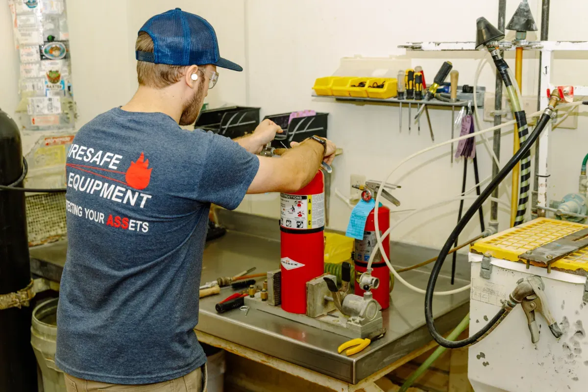 A man in a blue shirt is working on a fire extinguisher.