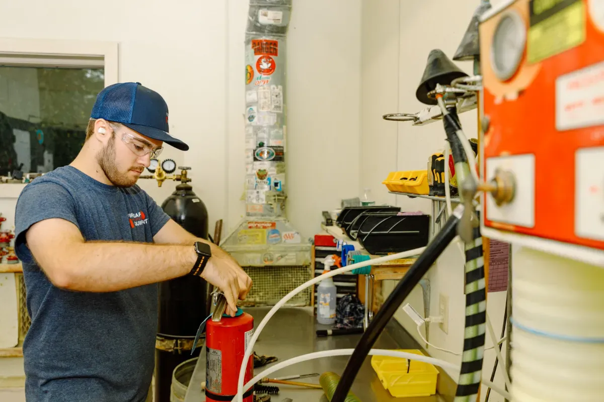 A man is working on a fire extinguisher in a workshop.