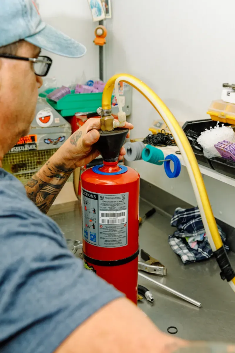 A man is working on a fire extinguisher with a yellow hose attached to it.