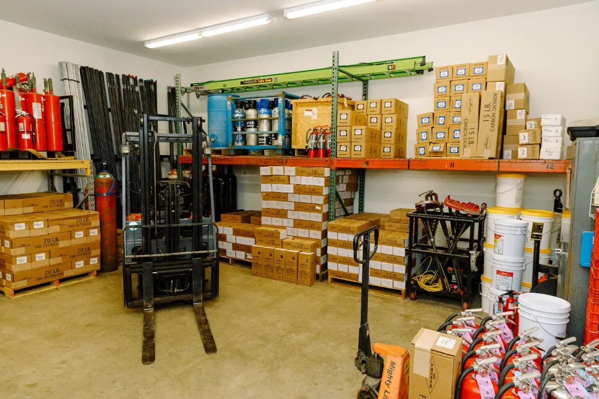 A forklift is sitting in a warehouse filled with boxes and fire extinguishers.