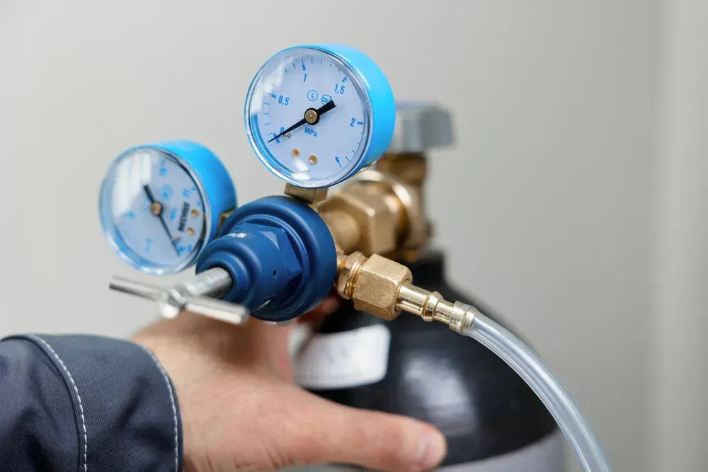 A person is holding a gas cylinder with a pressure gauge attached to it.