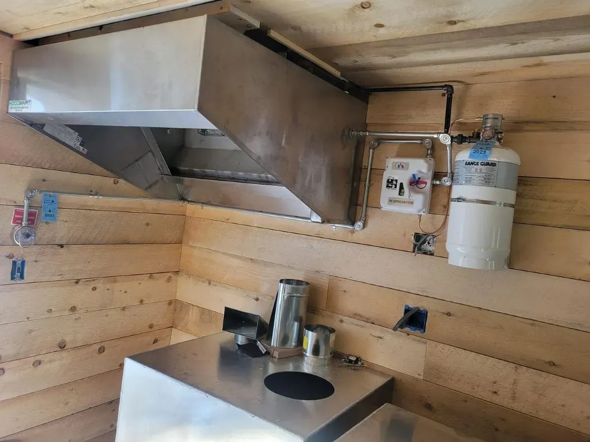 A kitchen with a stainless steel hood and a gas cylinder on the wall.
