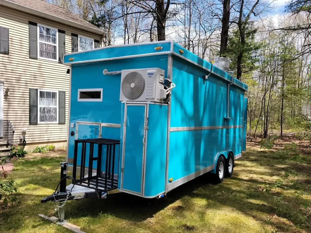 A blue trailer is parked in the grass in front of a house.