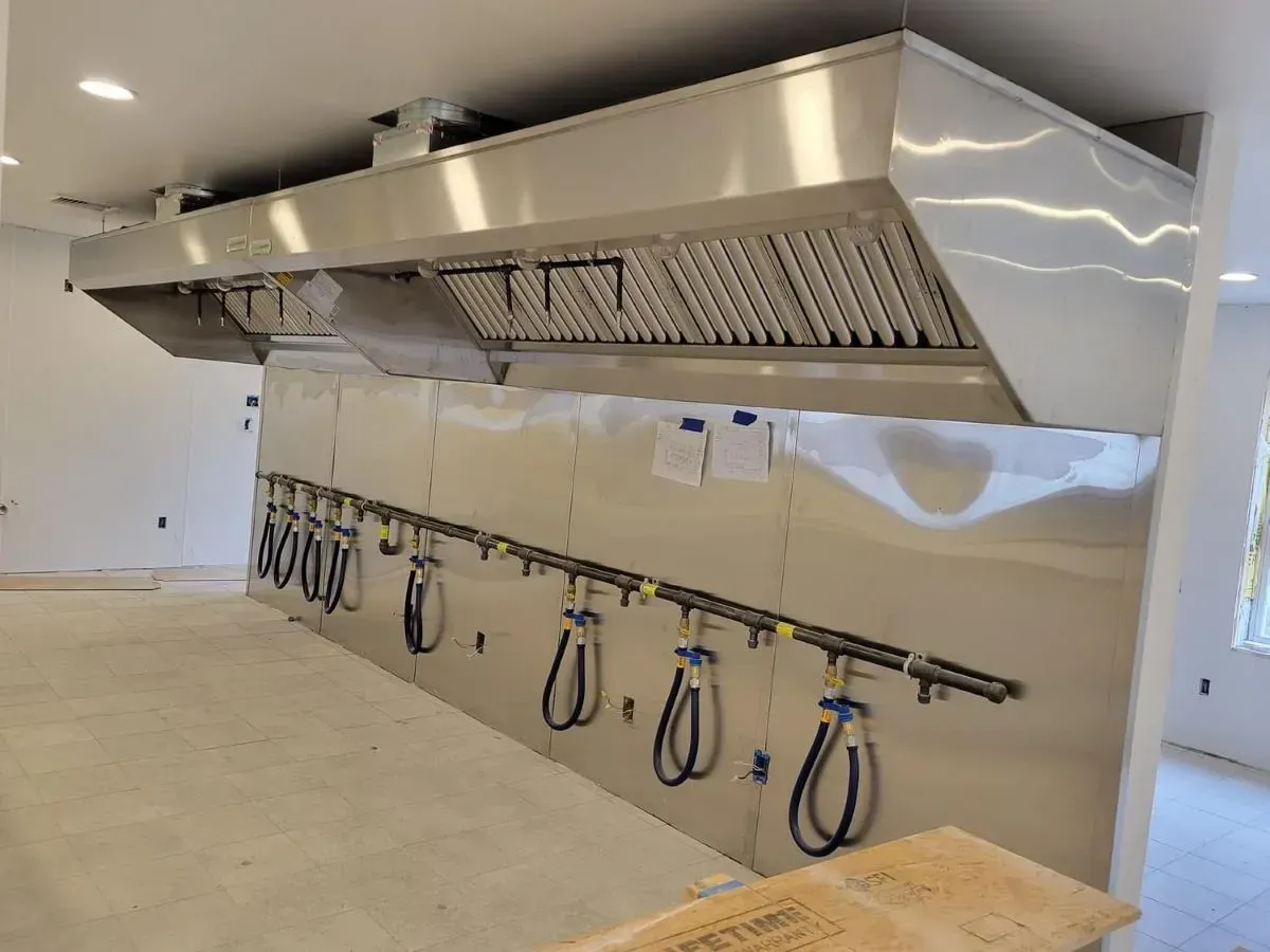 A stainless steel hood is hanging from the ceiling in a kitchen.