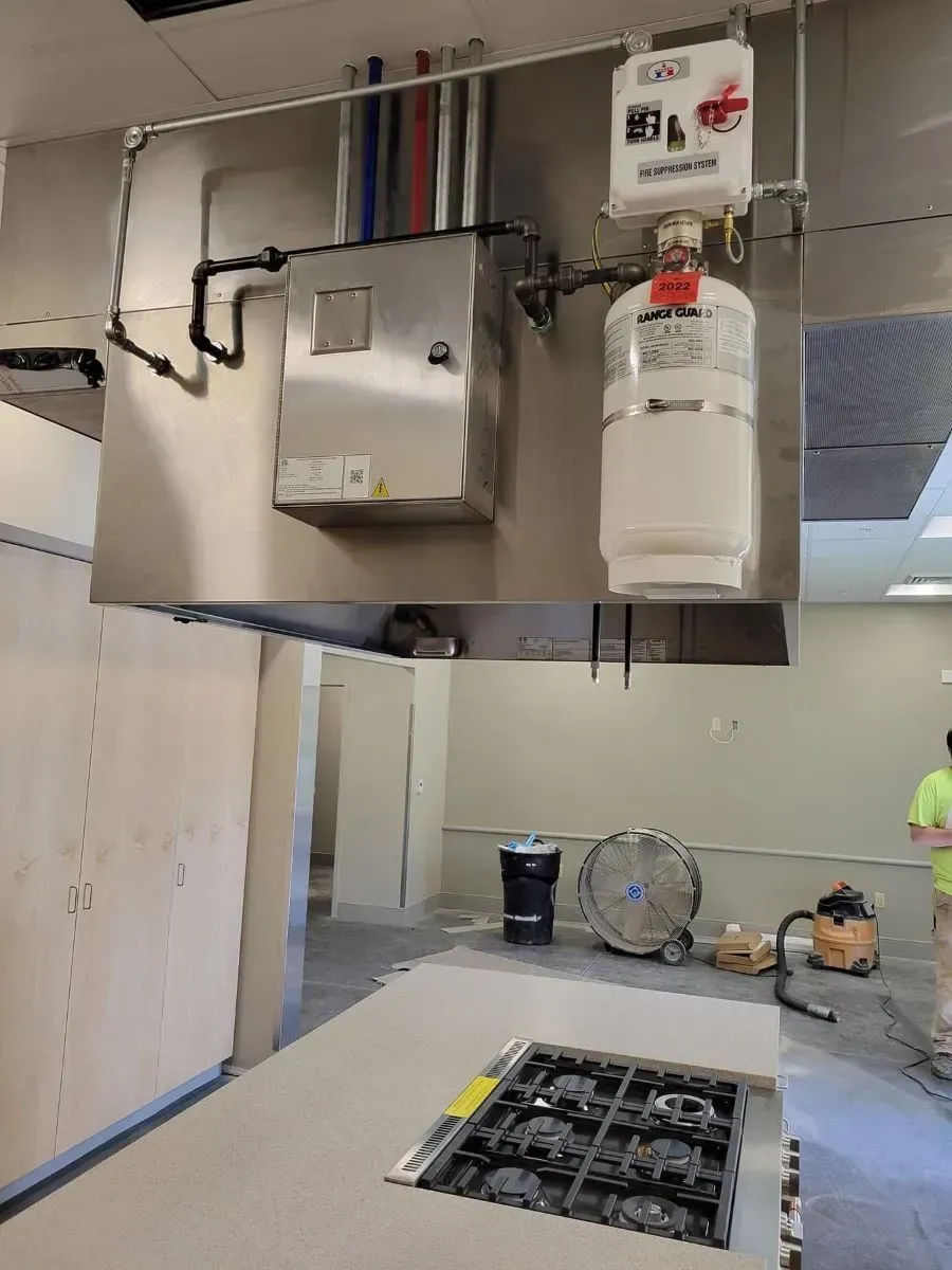 A kitchen with a stove and a gas cylinder hanging from the ceiling.