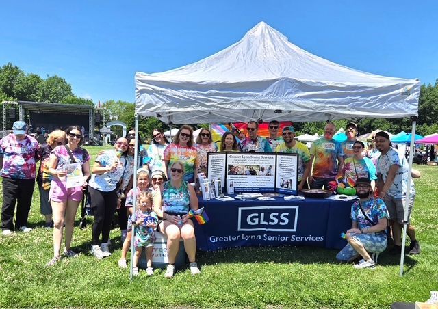 Group posing under white tent with GLSS banner at an outdoor event on a sunny day