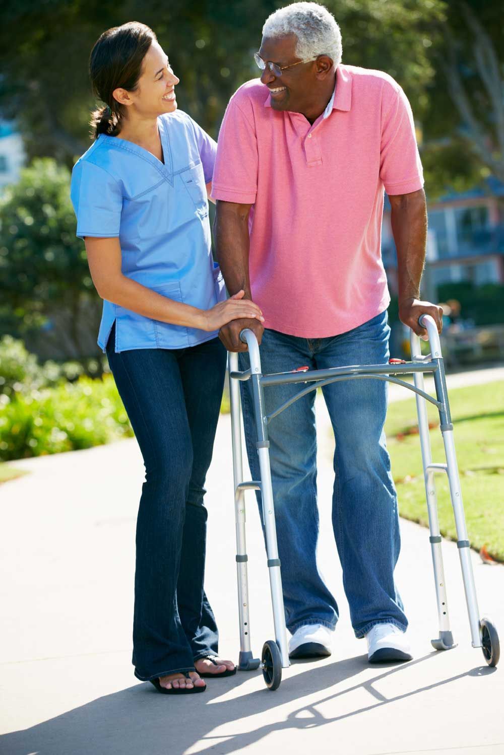 Two people talking outdoors beside a walker on a sunny sidewalk