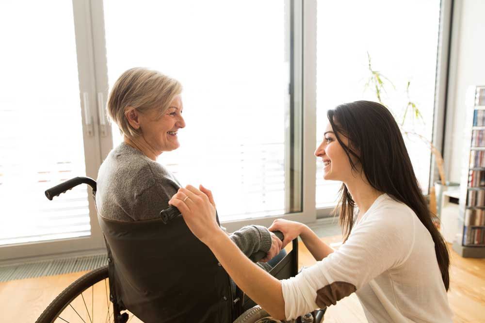 Elder in a wheelchair with a young woman talking to her.