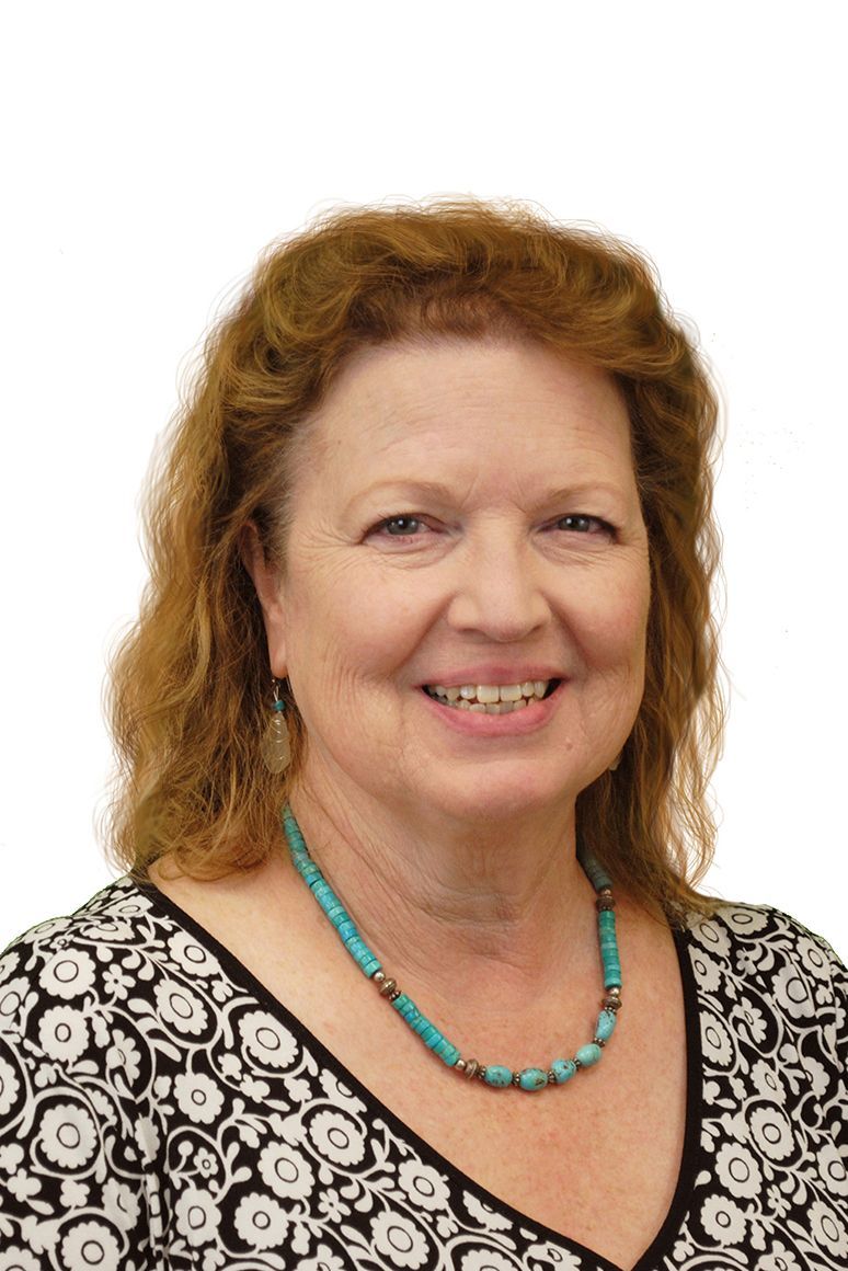 Woman with reddish-brown hair smiles, wearing a turquoise beaded necklace and patterned top.