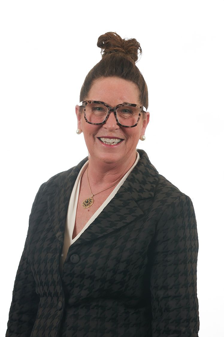 Smiling woman in glasses and a dark patterned blazer, photographed against a white background
