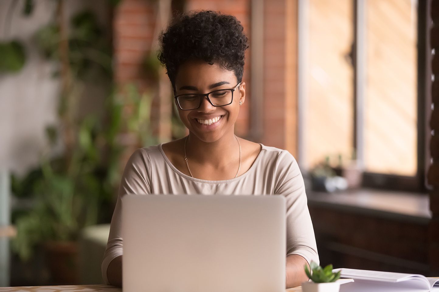Person smiling while using a laptop at a table in a bright indoor setting
