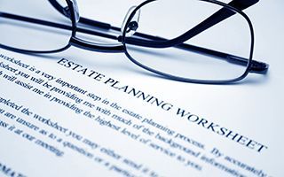 Estate planning worksheet under black eyeglasses on a blue desk.