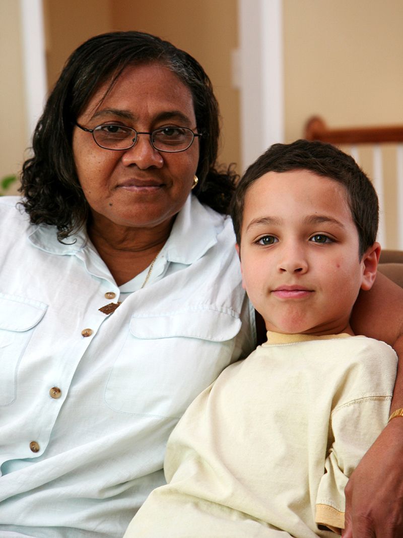 Woman in white coat seated with a child, both looking at the camera indoors.