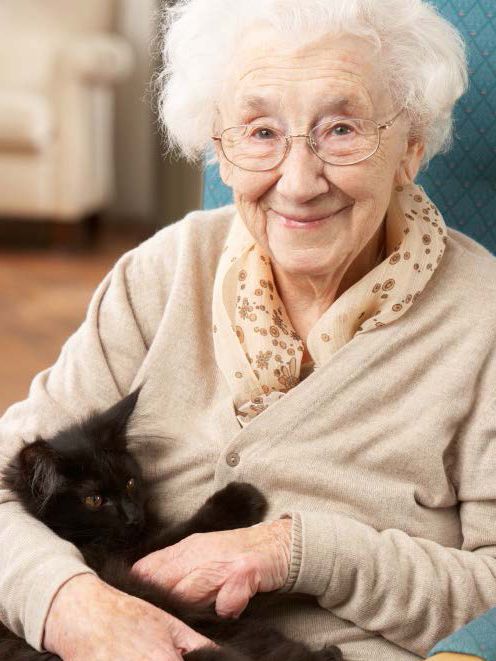 An older woman holding a black cat in her lap.