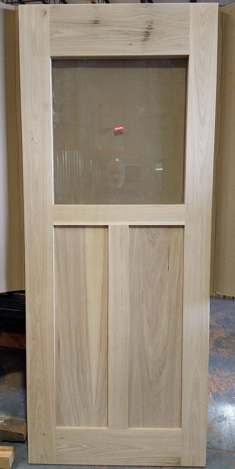 A wooden door with a glass window is sitting on a concrete floor.