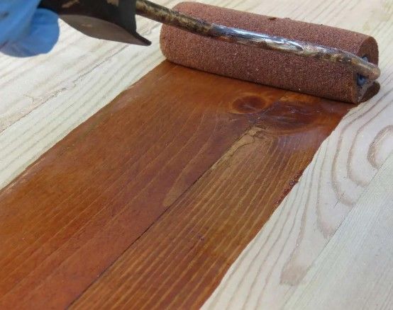 A person is painting a piece of wood with a roller.