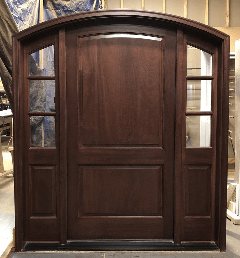 A large wooden door with arched windows is sitting in a room.