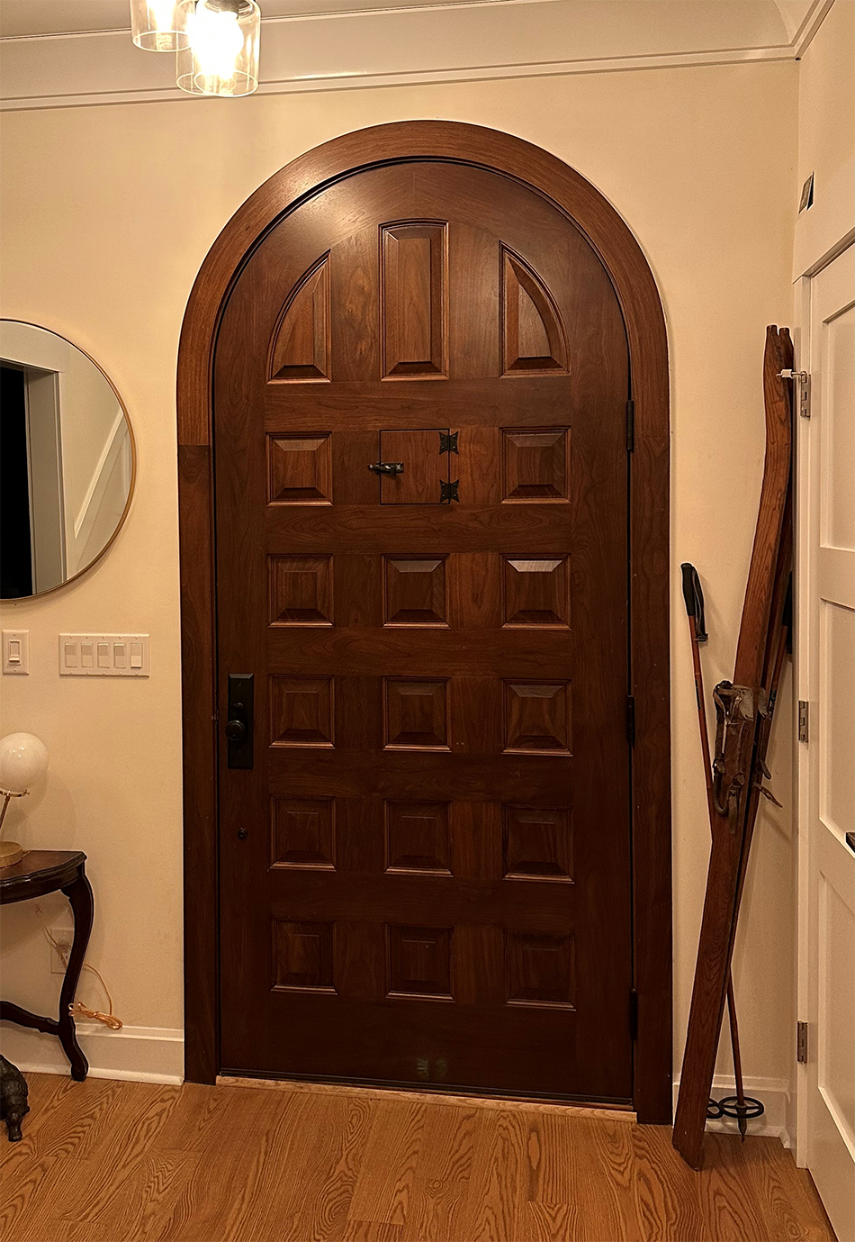 A large wooden door is in a hallway next to a mirror.