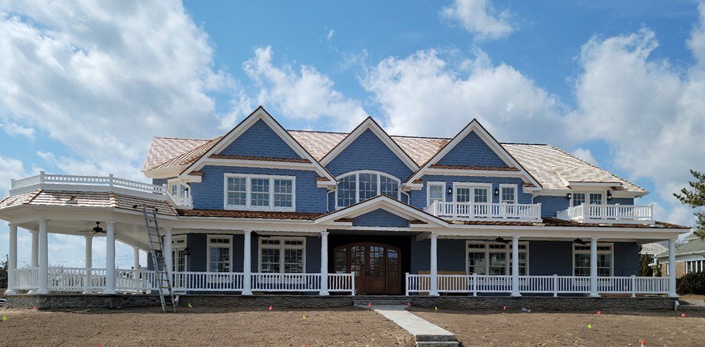 A large blue house with a white porch and a blue sky in the background.