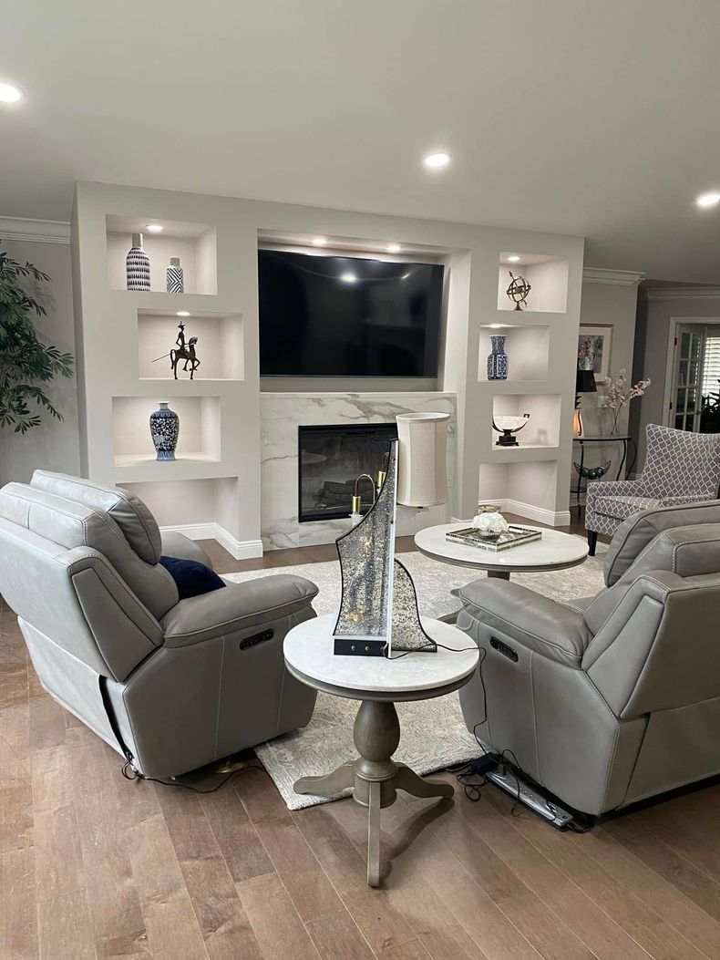 Modern living room with white fireplace, wall-mounted TV, and two gray recliners around a round table