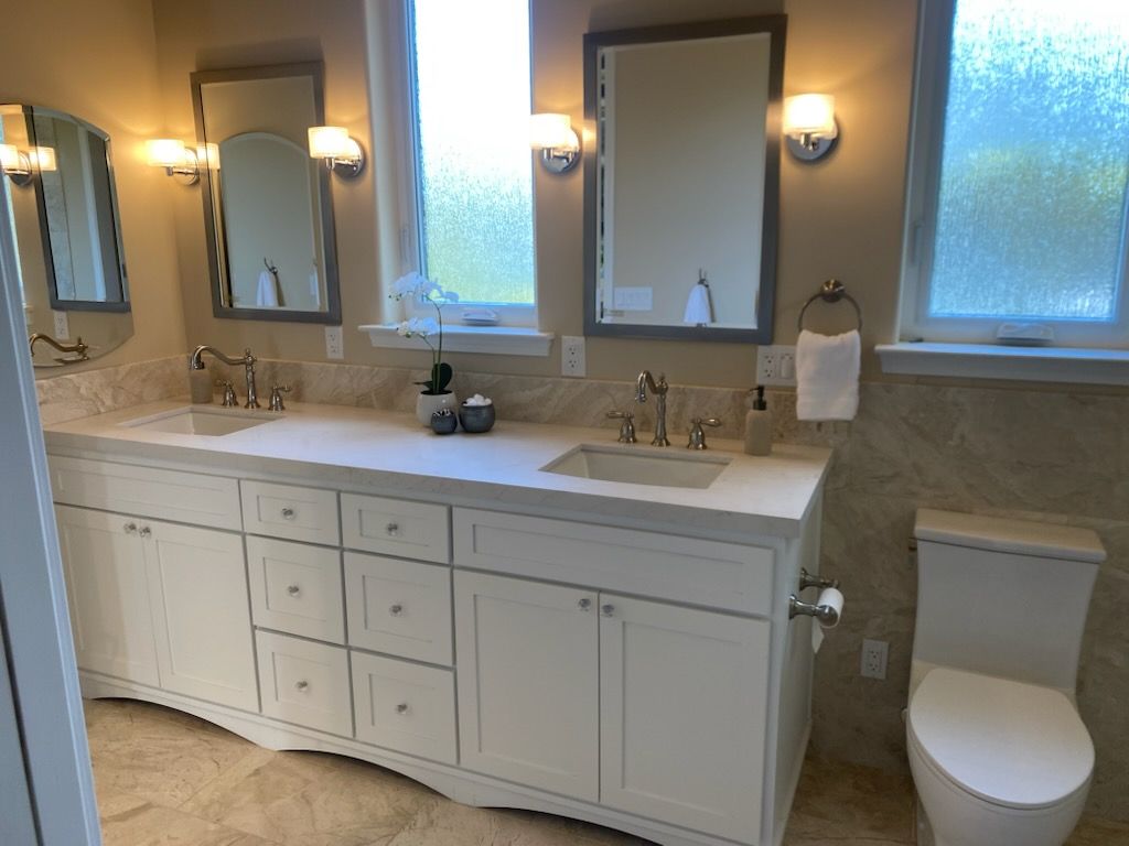 Modern bathroom with double vanity, mirrors, sconces, frosted window, and toilet on the right.