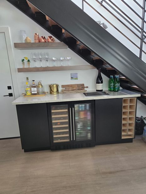 Under-stairs home bar with shelves, mini fridges, bottles, and a countertop in a modern room