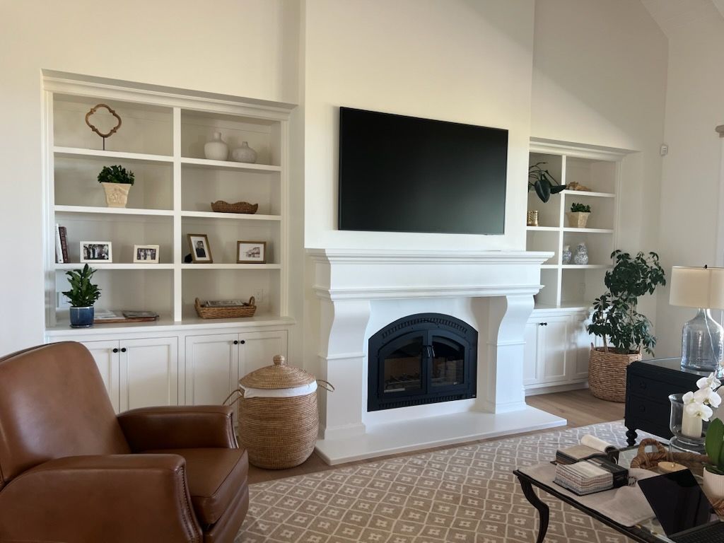 Living room with white built-in shelves, fireplace, TV, tan chair, and woven baskets