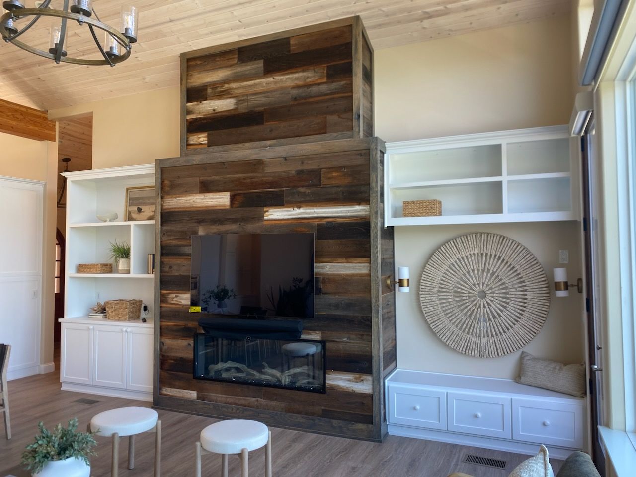 Living room with built-in white shelves, rustic wood TV wall, and two small stools in front